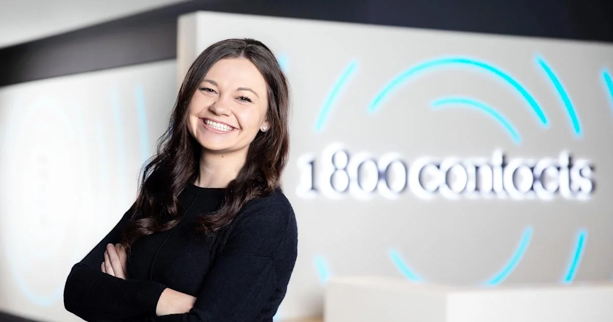 A smiling 1-800 Contacts team member in front of the lit company sign, for a guide on where to buy contact lenses online