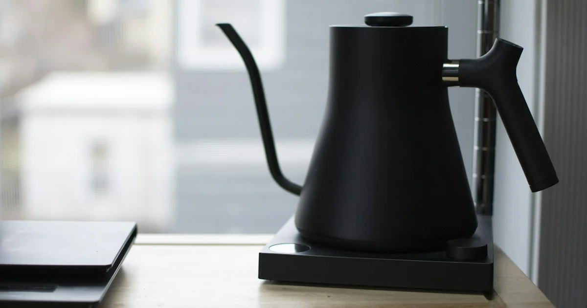 Black electric gooseneck kettle on its powered base by a kitchen window, a pour-control shape to consider for the best electric kettle 2026