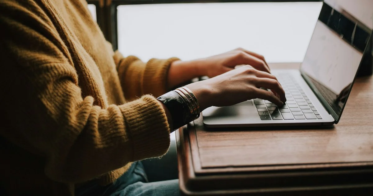 Hands typing on a laptop at a wooden desk beside a window, the daily inbox work that decides the best email client 2026 to choose