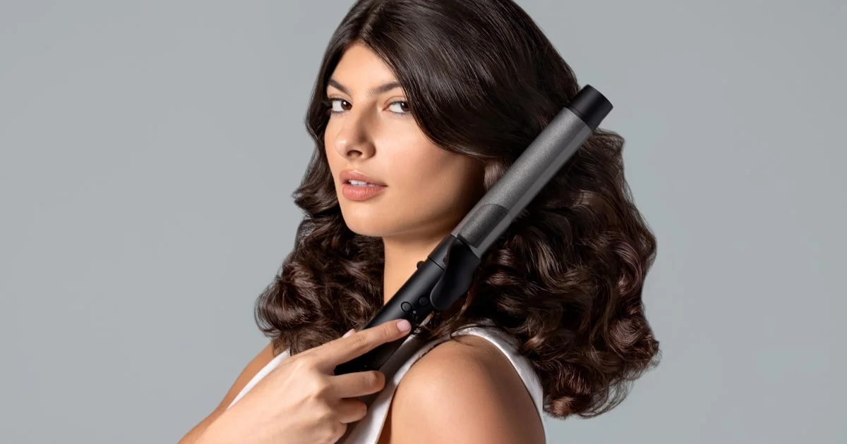 Woman holding a black curling iron wand up to her curled hair