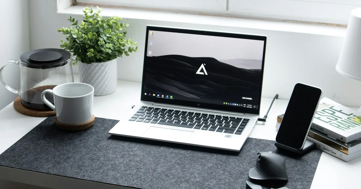 A home office desk with a laptop on a stand, a phone dock, a mug and a small speaker