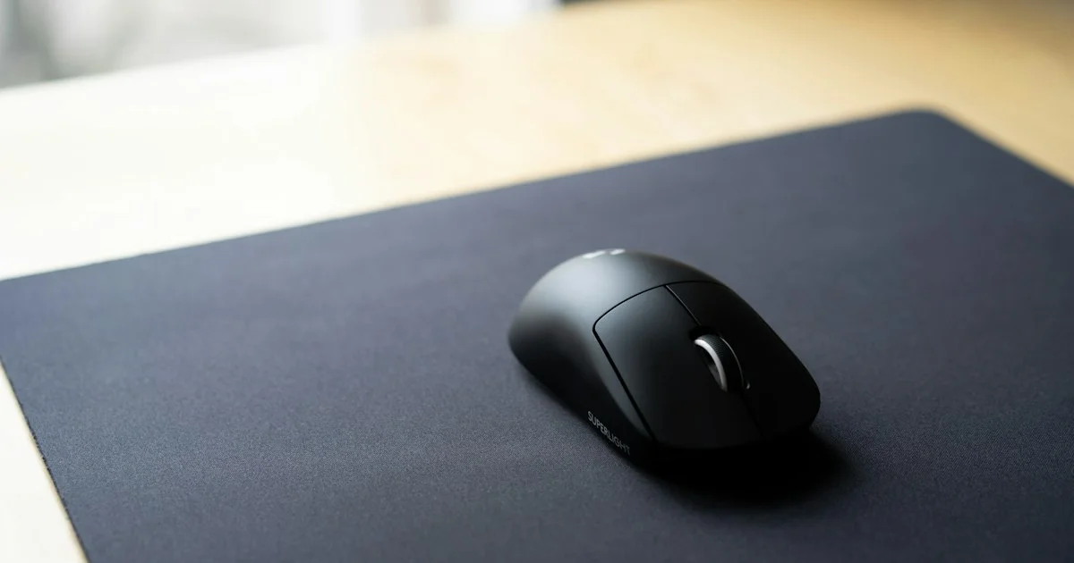 Large black cloth gaming mouse pad on a wooden desk with a wireless gaming mouse on it