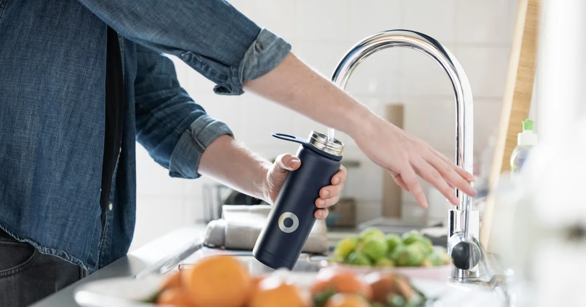Person filling a reusable water bottle at a kitchen sink for daily hydration