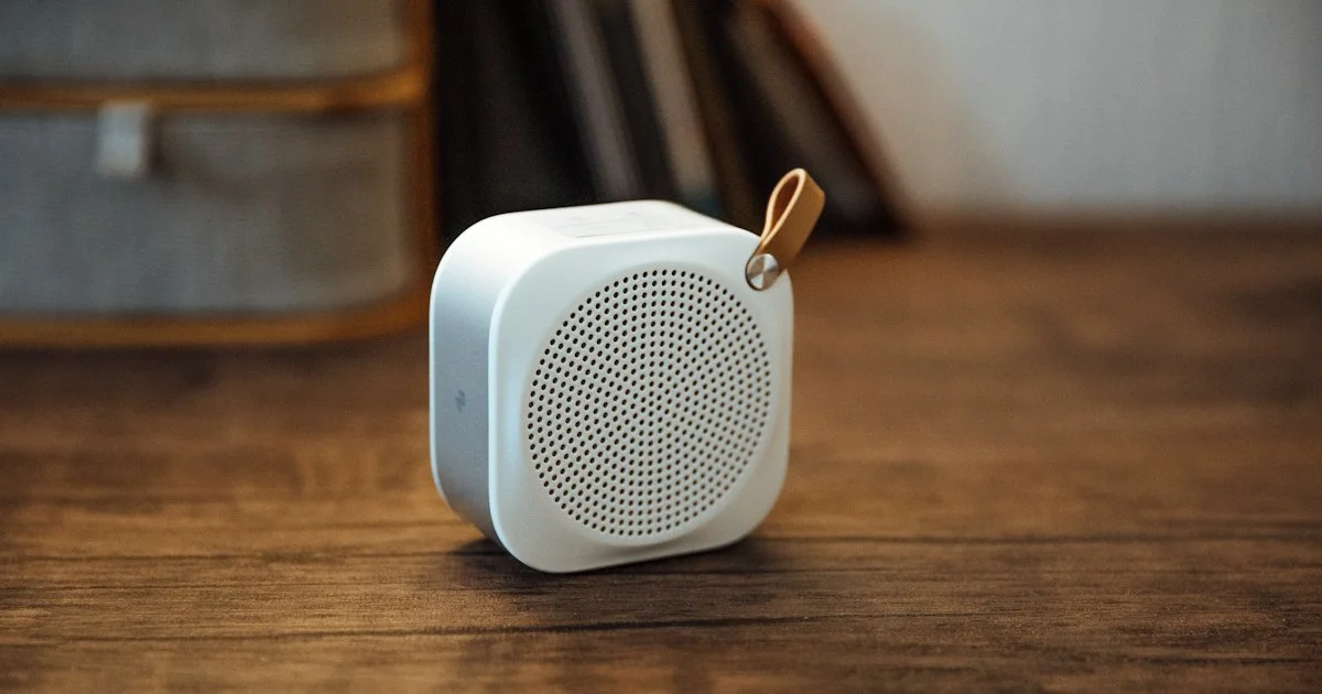 Small white portable Bluetooth speaker with a carry loop on a wooden table, the compact size to weigh up when working out how to buy a bluetooth speaker
