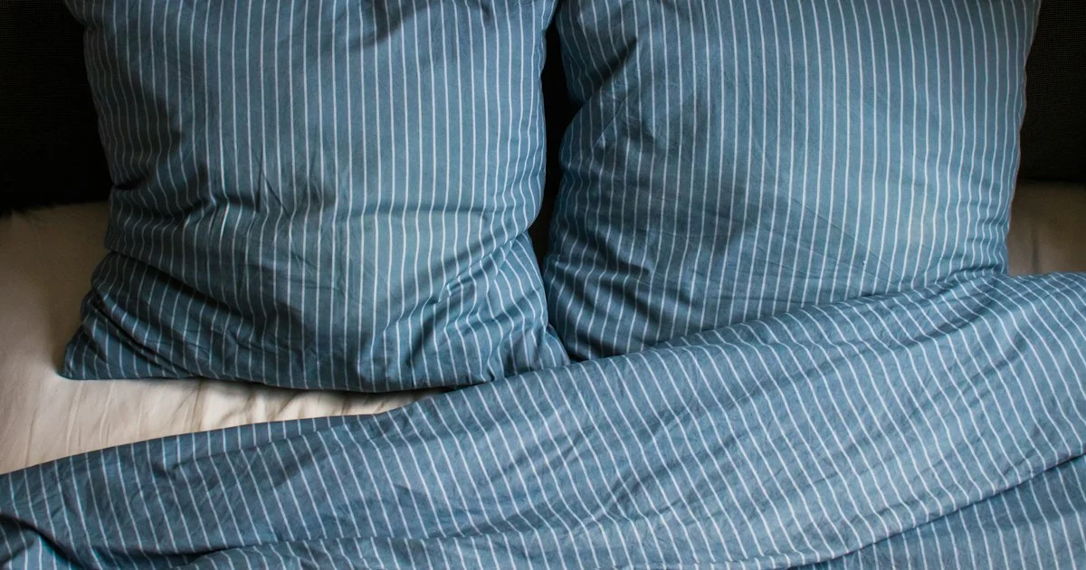Two ordinary pillows in blue striped cases on a made bed, the everyday object underneath any decision about how to buy a smart pillow