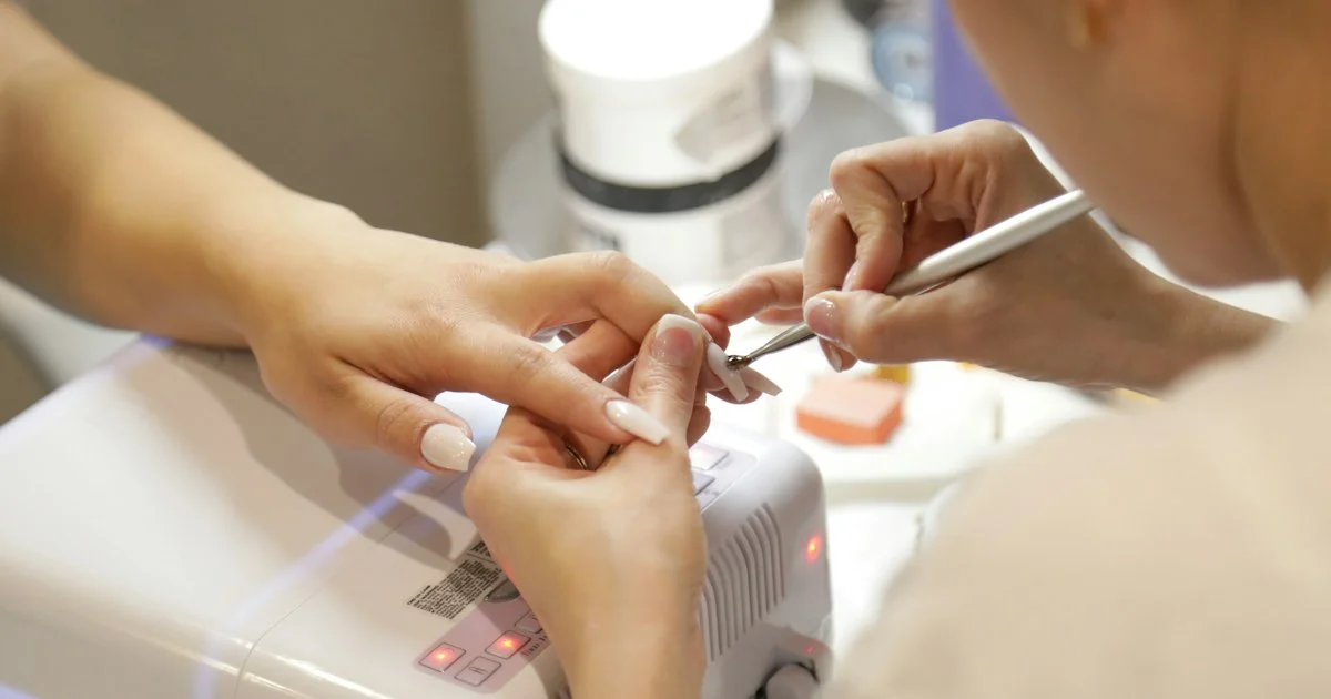 A nail curing lamp glowing over a hand at a salon table, the device at the center of how to buy a UV nail lamp