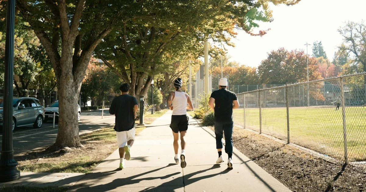 Three runners on a sunny sidewalk beside a road, the setting that decides how to choose a running headphones pair