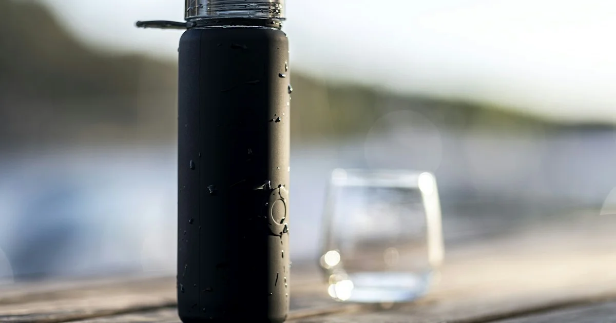 A matte black insulated bottle beside a plain glass of water, illustrating how to choose a smart water bottle