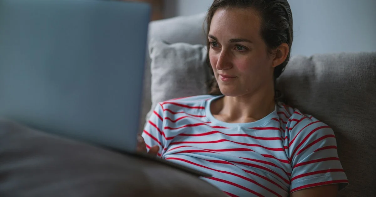 A woman watching a laptop screen while lying on a sofa, the small-screen evening that shapes how to choose a smart AR glasses setup