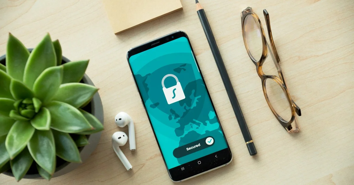 A smartphone on a desk showing a lock screen for a secured app, beside glasses and earbuds