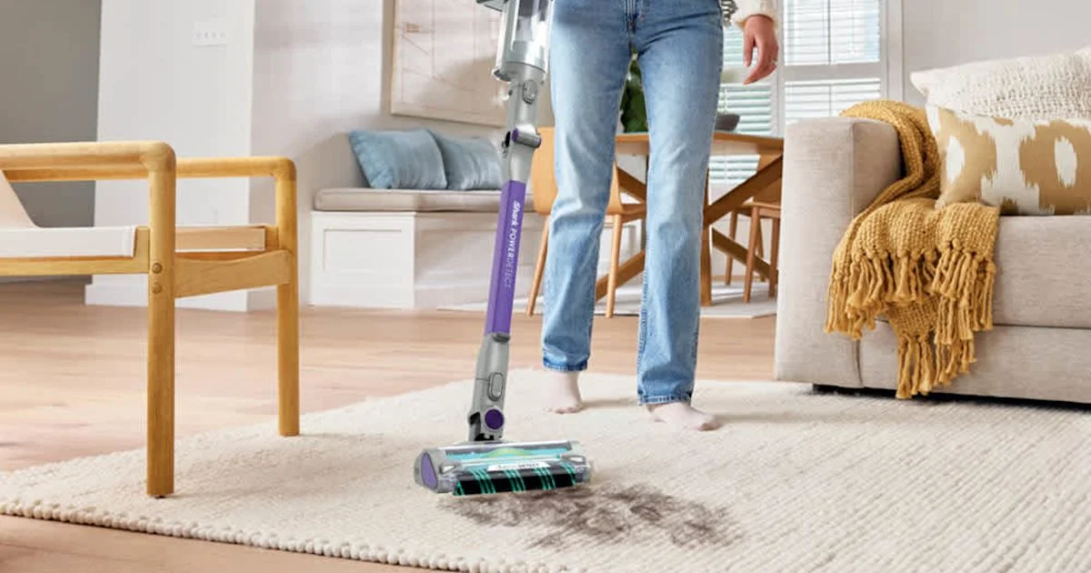 A Shark PowerDetect cordless stick vacuum cleaning a woven rug in a living room, a key comparison in how to choose a cordless stick vacuum