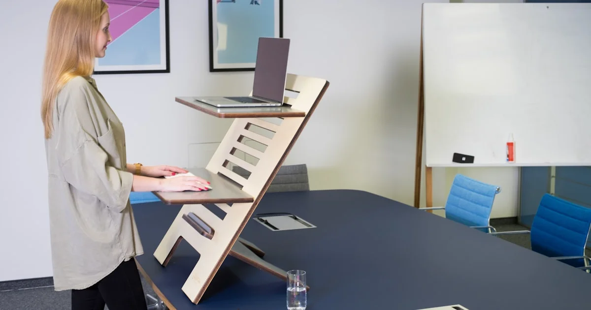 Person standing while working at a standing desk converter placed on top of a home office desk