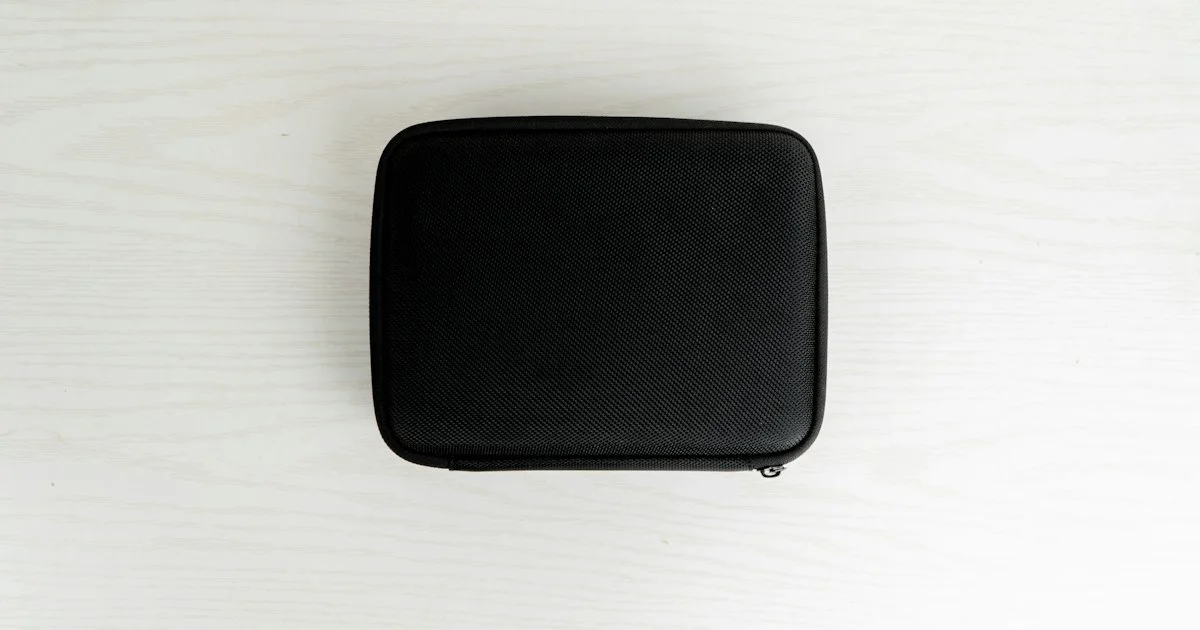 A plain black zip-around tech case on a pale desk, the shape to look for in a top cable organizer bag 2026
